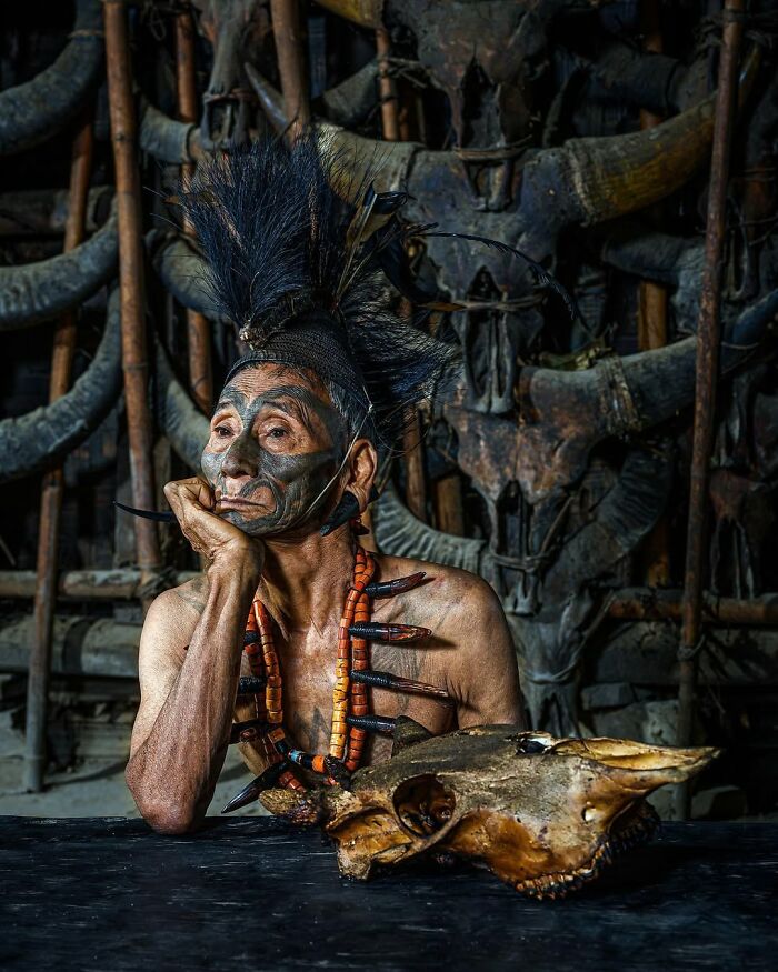 Hombre mayor con pintura facial y tocado tradicional, retrato elocuente de personas mayores en entorno cultural único.
