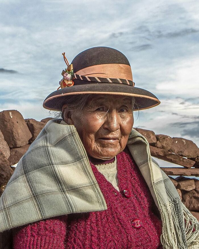Retrato elocuente de persona mayor con sombrero tradicional y chal, en entorno rural, destacando rasgos y expresión auténtica.