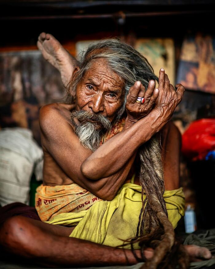 Hombre mayor con cabello largo y enredado en pose meditativa, retrato elocuente de personas mayores en el mundo.