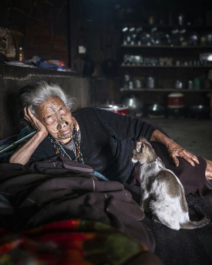 Anciana mayor con tatuajes faciales tradicionales recostada junto a un gato en retrato elocuente de personas mayores.