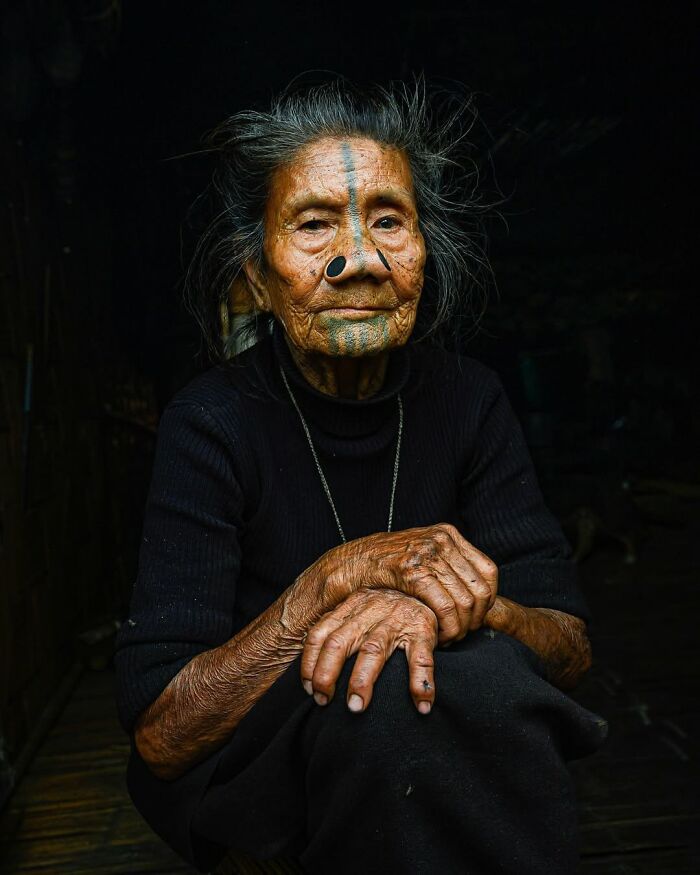 Retrato elocuente de persona mayor con tatuajes faciales y nariz perforada, representando diversidad cultural mundial.
