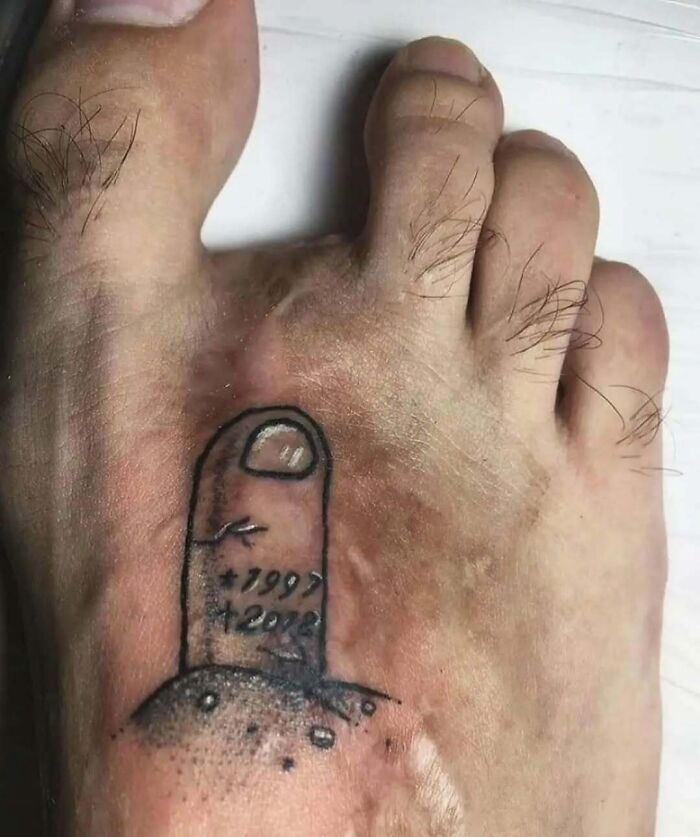 Tatuaje gracioso en pie que simula una uña enterrada con fechas, ejemplo de tatuajes que van de lo gracioso a lo terrible.