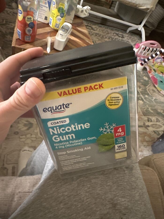 Mano sosteniendo paquete grande de chicles de nicotina en ambiente casero, entre cosas desordenadas.