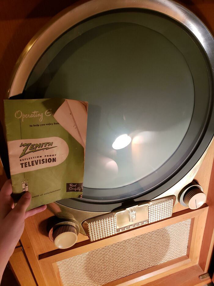 Televisor antiguo Zenith redondo con manual de instrucciones sostenido a un lado, mostrando comparación temporal vintage.