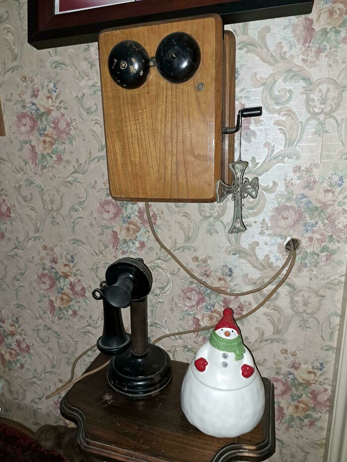 Teléfono antiguo de madera y metal junto a adorno de muñeco de nieve mostrando comparación temporal.
