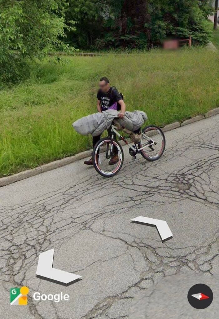 Hombre con bicicleta en calle agrietada junto a césped, uno de los lugares misteriosos encontrados en Google Earth.