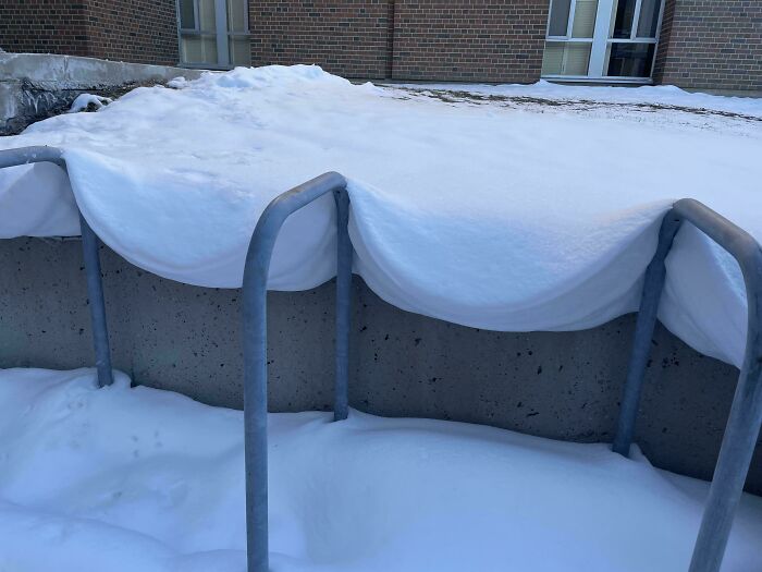 Nieve acumulada en barandilla de metal formando una figura que parece una manta doblada, objetos interesantes que parecen otras cosas.