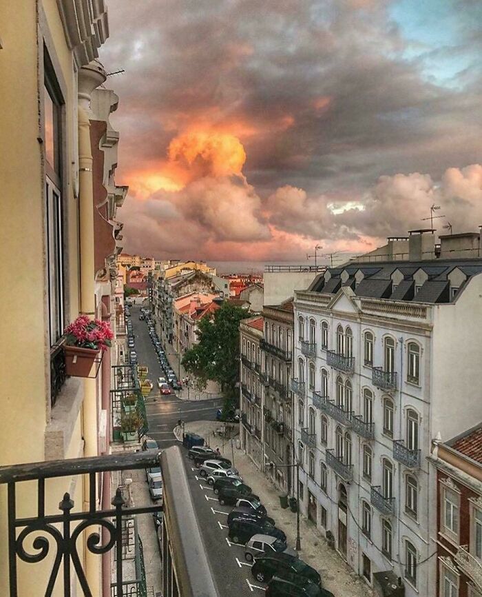Cielo al atardecer con nubes que parecen formas interesantes sobre una calle urbana con edificios y coches estacionados.