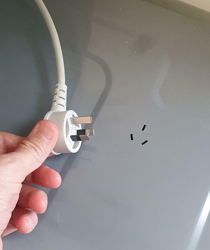 Mano sosteniendo enchufe blanco en fondo gris, ilustrando soluciones geniales a problemas habituales en el hogar.