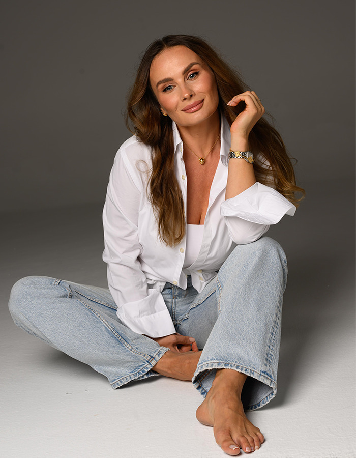 Cosmetóloga femenina con cabello largo en camisa blanca y jeans, representando belleza natural sin procedimiento cosmético en Hollywood.