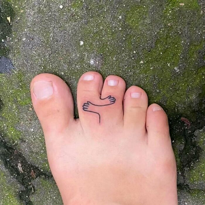 Tatuaje divertido de brazos abrazando los dedos del pie, ejemplo de personas que decidieron hacerse tatuajes creativos y únicos.