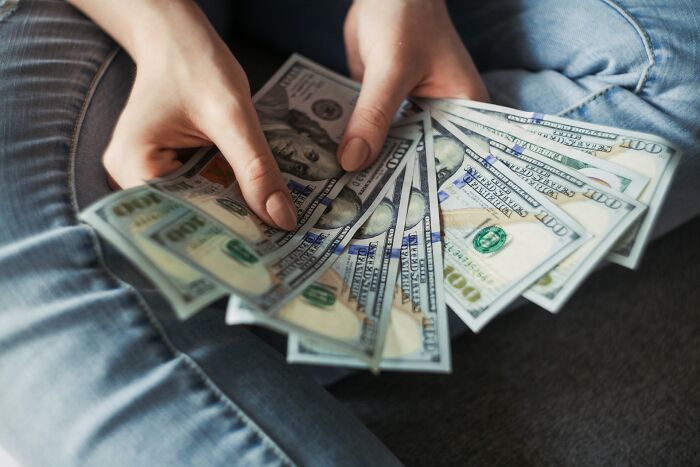 Manos sosteniendo billetes de dólares, ilustrando trucos vitales para ahorrar dinero y mejorar finanzas personales.