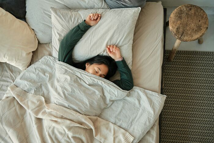 Persona única durmiendo en cama con ropa de cama beige y gris, mostrando tranquilidad y descanso en ambiente hogareño.