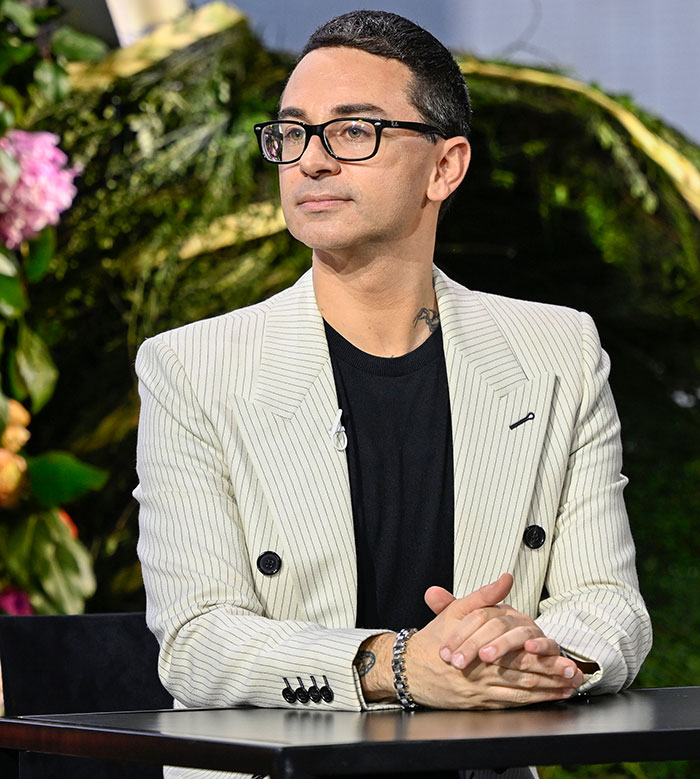 Hombre con gafas y chaqueta blanca de rayas sentado en mesa, en un evento con momentos incómodos de la Gala Met 2025.
