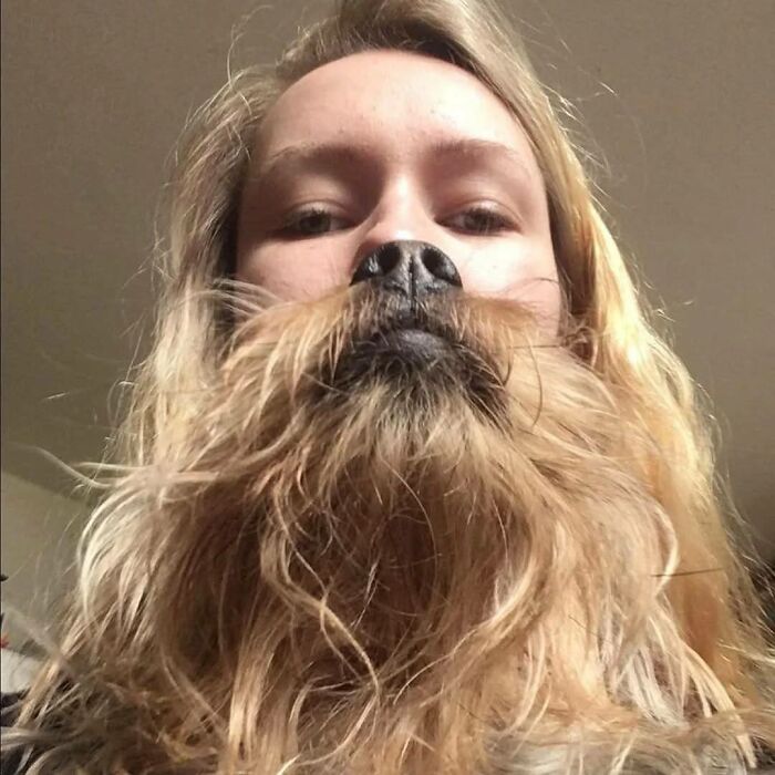 Mujer con cabello rubio que parece tener barba de perro gracias a la posición de su mascota en una foto divertida y sorprendente.