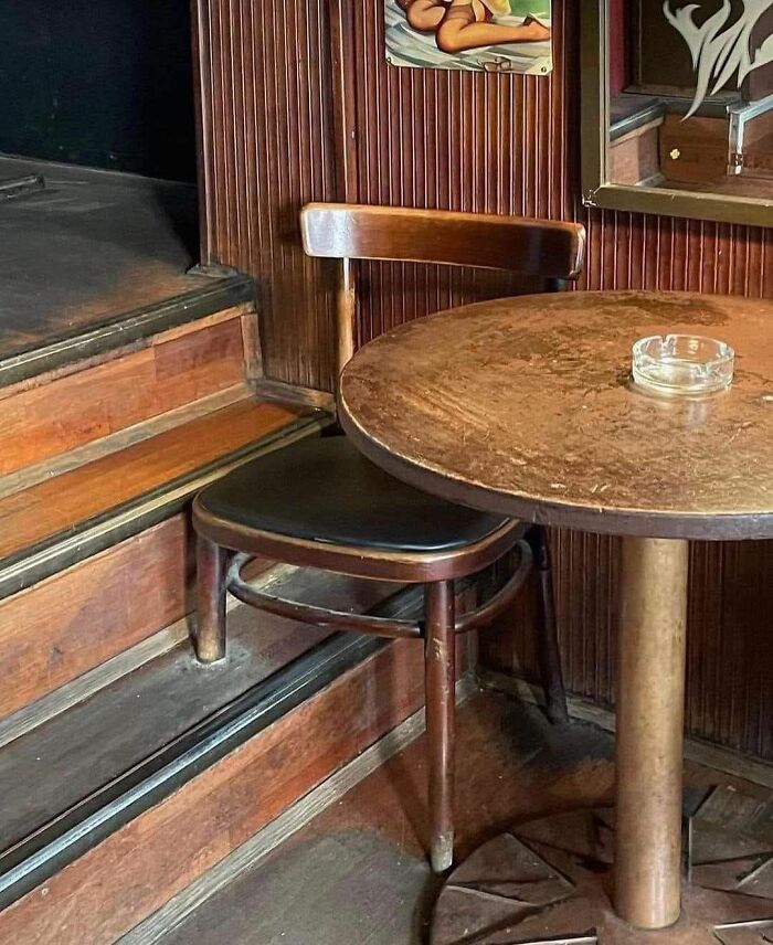 Silla colocada en escalón junto a mesa redonda y cenicero en ambiente de madera antiguo, imagen curiosa para personas que hicieron una foto