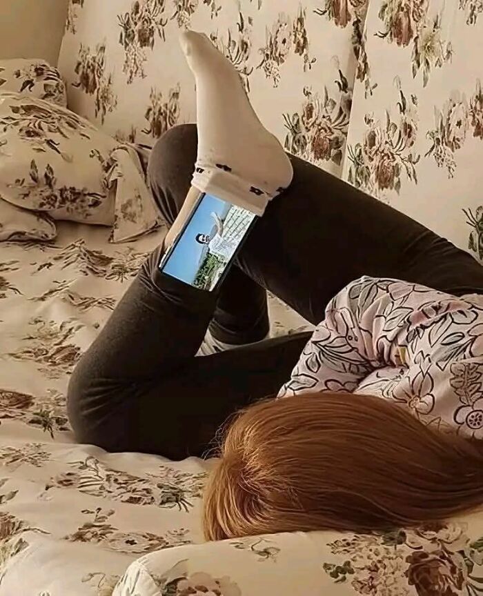 Persona viendo un video en el teléfono móvil sostenido entre pierna y pie, imagen curiosa capturada en foto.