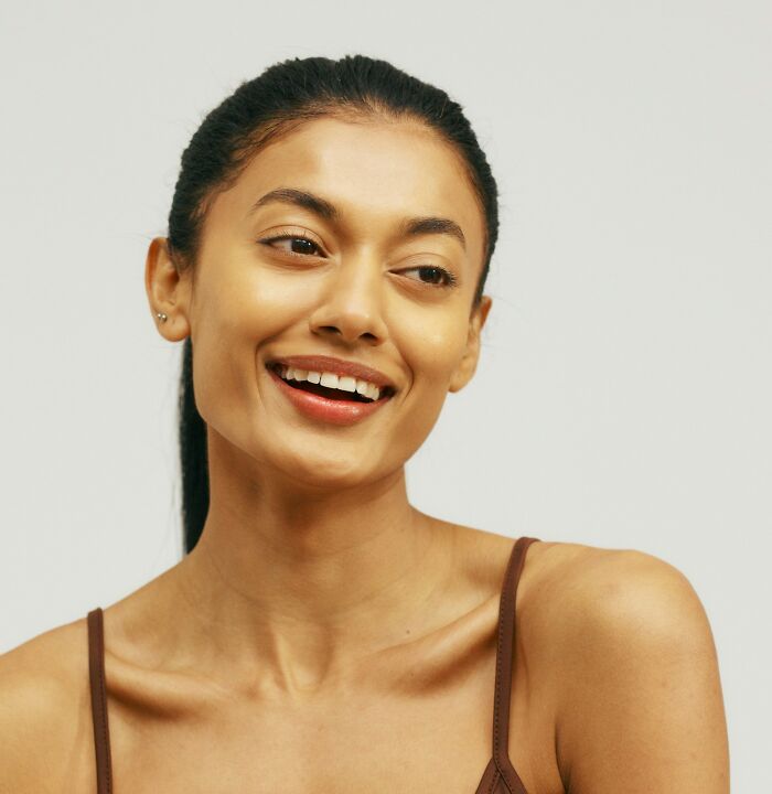 Mujer joven con expresión sonriente mostrando buenos genes y rasgos naturales en fondo claro.