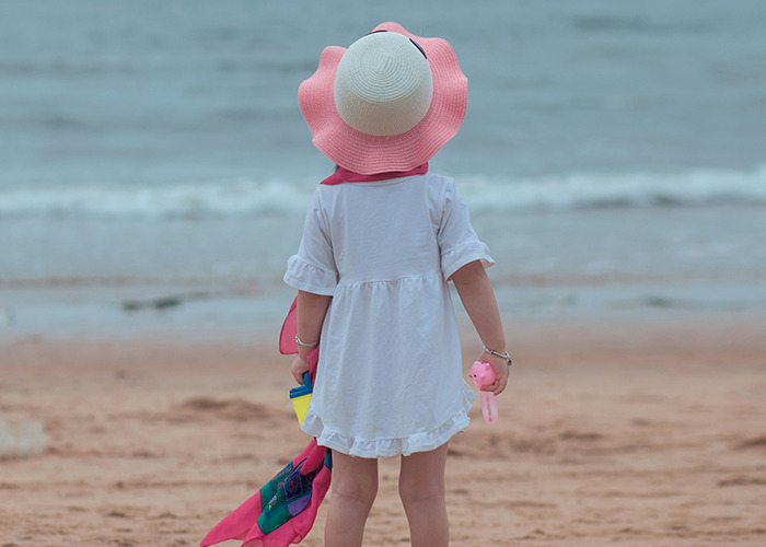Niña de espaldas en la playa con sombrero rosa, ilustrando consejos vitales del personal sanitario y de emergencias.