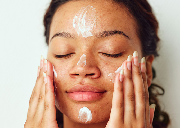 Mujer aplicando crema facial con ojos cerrados cuidando la piel siguiendo consejos del personal sanitario y de emergencias.