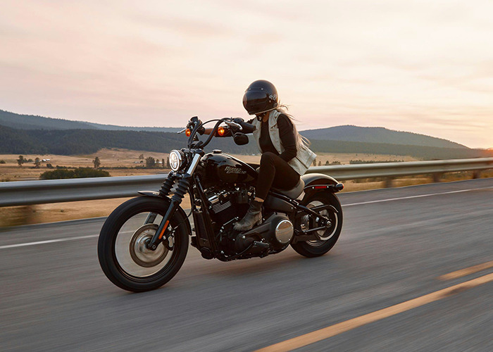 Mujer en moto con casco conduce sobre carretera al atardecer siguiendo consejos vitales de personal sanitario y emergencias.