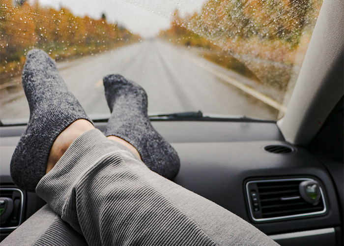 Persona con calcetas grises y pantalones relajados dentro de un coche en carretera lluviosa, consejos vitales de emergencias