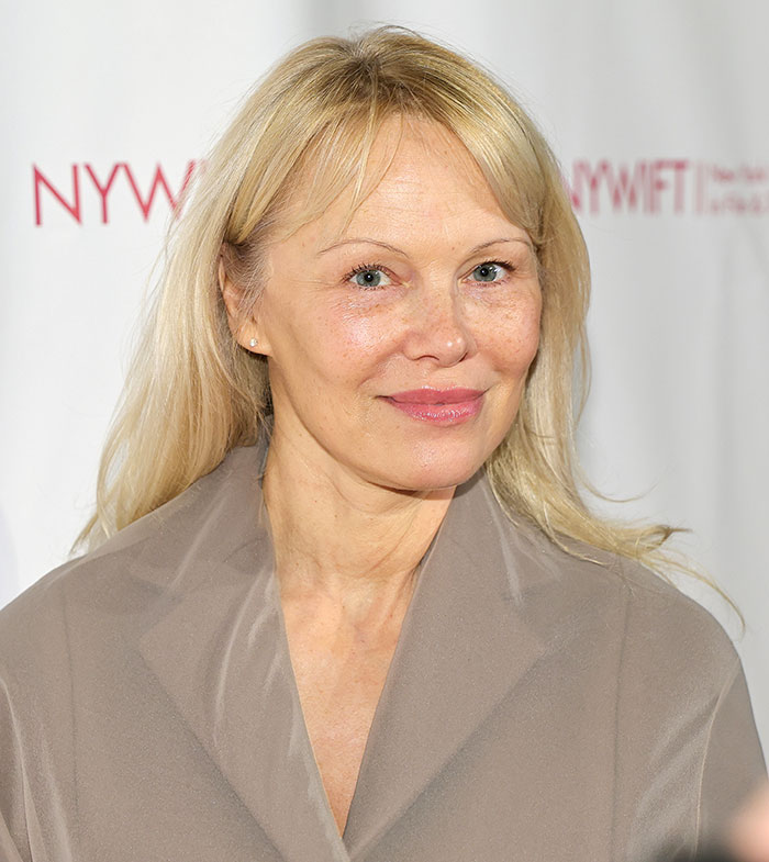 Pamela Anderson con look natural y maquillaje minimalista en evento interior mostrando estilo glamuroso de los 90