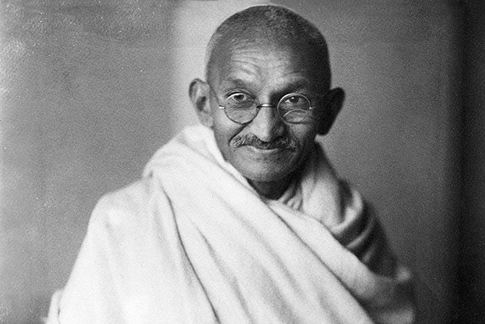 Hombre mayor con gafas redondas y túnica blanca en primer plano, imagen en blanco y negro de celebridades problemáticas.