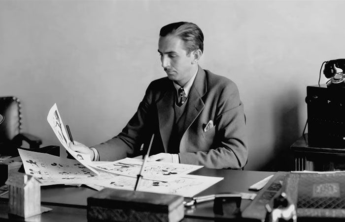 Hombre leyendo dibujos animados clásico sentado en escritorio, representando celebridades problemáticas en historia humana.