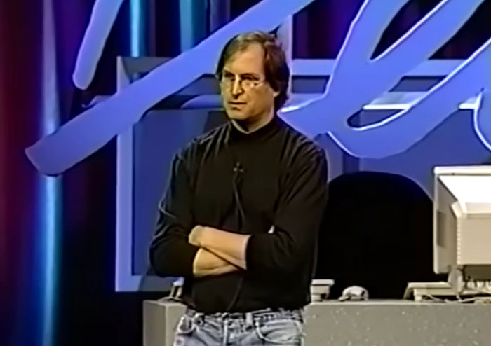 Hombre con camiseta negra de manga larga y jeans hablando frente a audiencia sobre celebridades problemáticas en un evento.