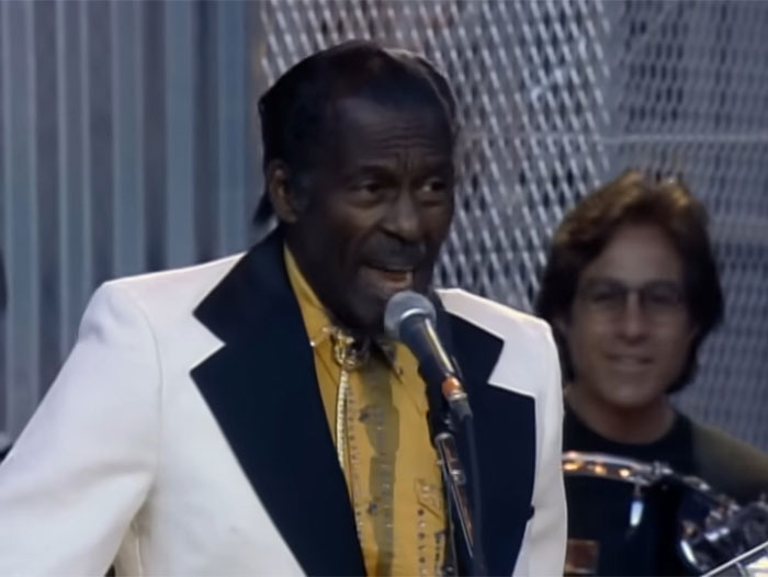 Cantante famoso problemático interpretando en vivo con chaqueta blanca, ilustrando celebridades problemáticas y seres humanos horribles.
