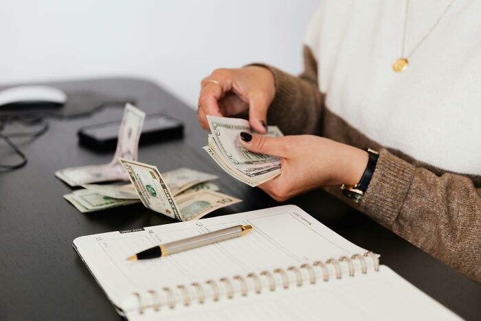 Persona contando billetes en escritorio con agenda abierta representando la lotería genética y características únicas