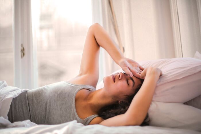 Mujer descansando en cama al despertar usando trucos vitales para mejorar su día a día en habitación iluminada.