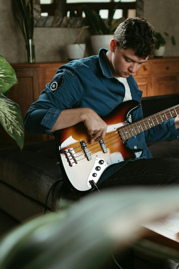 Joven tocando bajo eléctrico sentado en sala con plantas, resaltando la lotería genética en personas únicas.