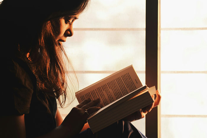 Mujer leyendo en silencio junto a ventana, reflejando momentos de reflexión sobre pareja idiota.