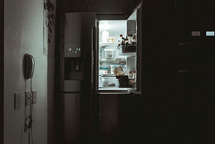Refrigerador abierto en cocina oscura simbolizando momentos de parejas que se han dado cuenta de que su pareja es idiota.