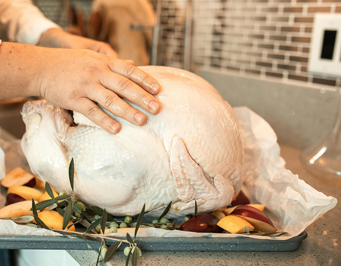 Manos preparando un pavo crudo con frutas y hierbas en bandeja, sorprendiendo a personas que descubren pareja idiota.
