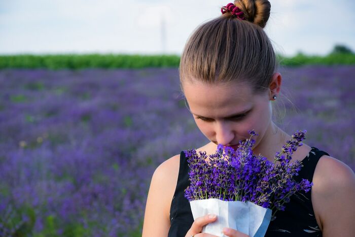 Mujer joven con recogido oliendo un ramo de flores moradas en un campo al aire libre, genes buenos o malos.