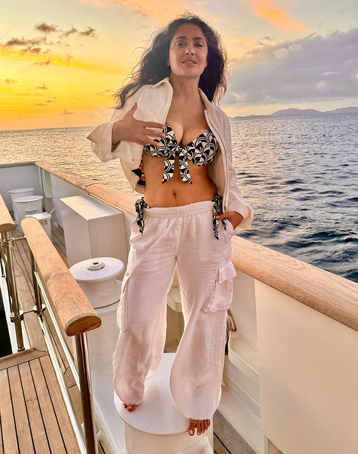 Salma Hayek en bikini negro y blanco con pantalones blancos posando en yate al atardecer para Sports Illustrated Swimsuit.