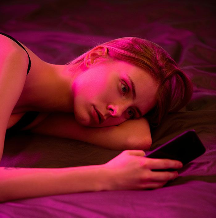 Mujer acostada con expresión triste mirando su celular, representando señales de infidelidad y desconfianza en la pareja.