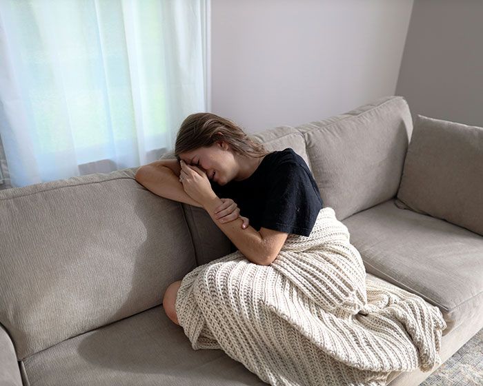 Mujer triste y cubierta con una manta en un sofá, mostrando señales de infidelidad y emociones ocultas.