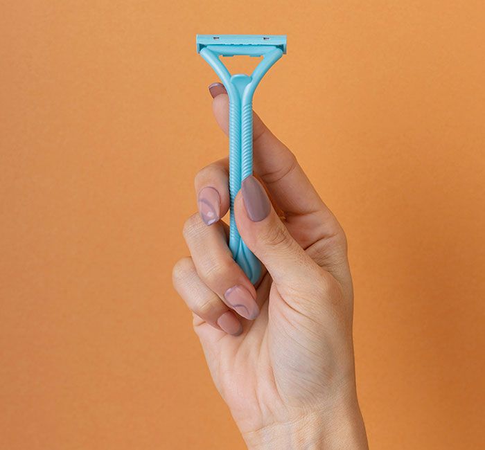 Mano sosteniendo una rasuradora azul sobre fondo naranja como posible señal de infidelidad oculta.