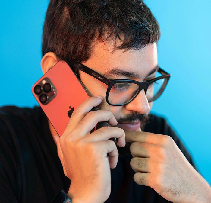 Hombre pensativo con gafas hablando por teléfono, señal de infidelidad que la gente pasó por alto, fondo azul.