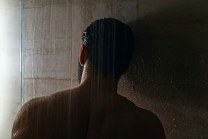 Hombre bajo la ducha de espaldas en ambiente oscuro, imagen que refleja señales de infidelidad sutiles y pasadas por alto.