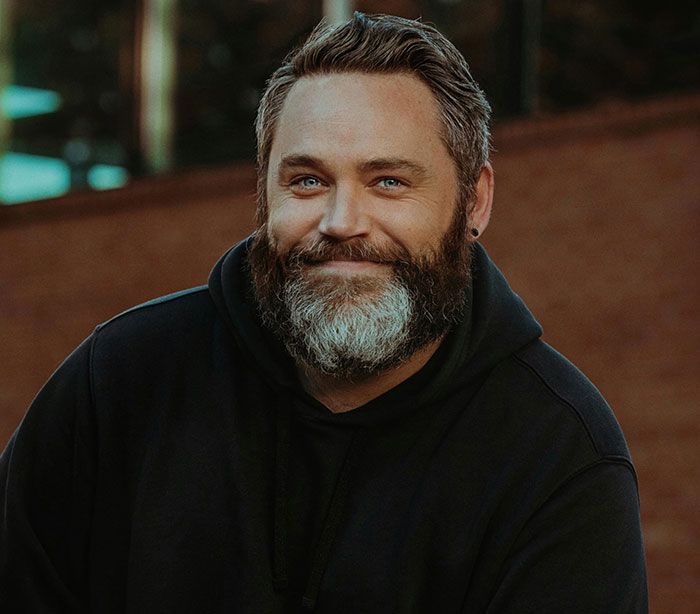 Hombre con barba y sudadera negra sonriente, ilustrando señales de infidelidad que a menudo se pasan por alto.
