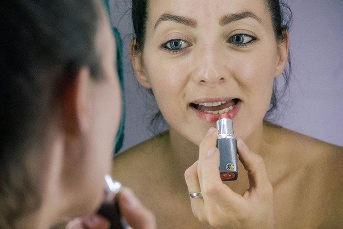 Mujer aplicándose brillo de labios frente al espejo mostrando señales de infidelidad que pasan por alto.