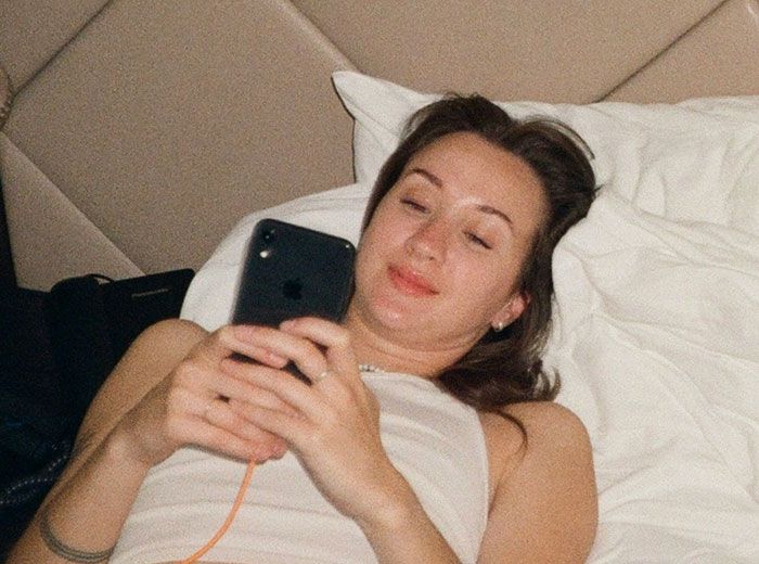 Mujer acostada en cama revisando su teléfono móvil, ilustrando señales de infidelidad ignoradas comúnmente.