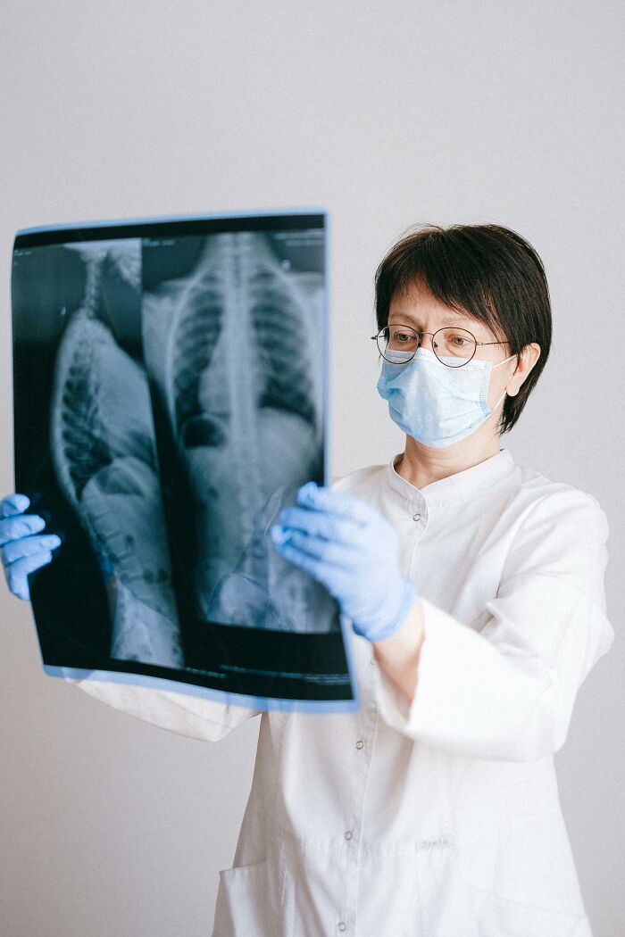 Doctora con mascarilla y guantes examinando radiografías, símbolo de lotería genética y análisis único de personas.