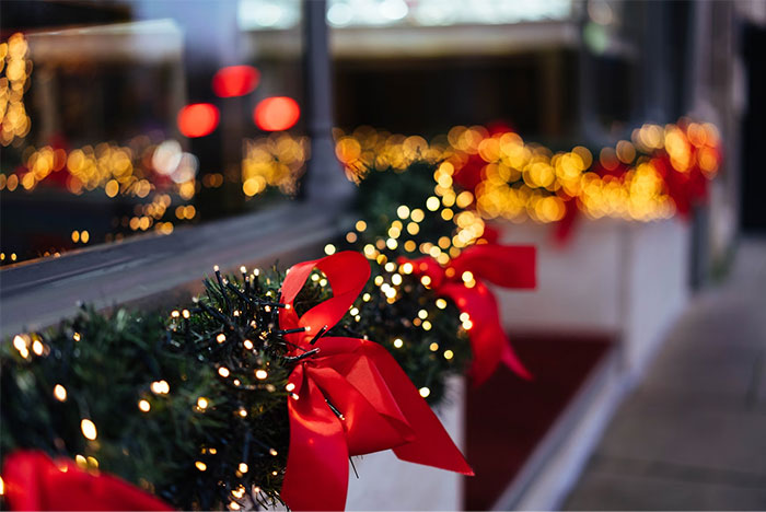 Guirnaldas decorativas con luces y lazos rojos detallando una ambientación navideña cerca de ventanas reflejando luces cálidas.