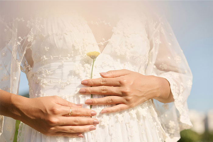 Manos de mujer con anillo sosteniendo una flor sobre vestido blanco de encaje, simbolizando historias sobre bodas inesperadas.